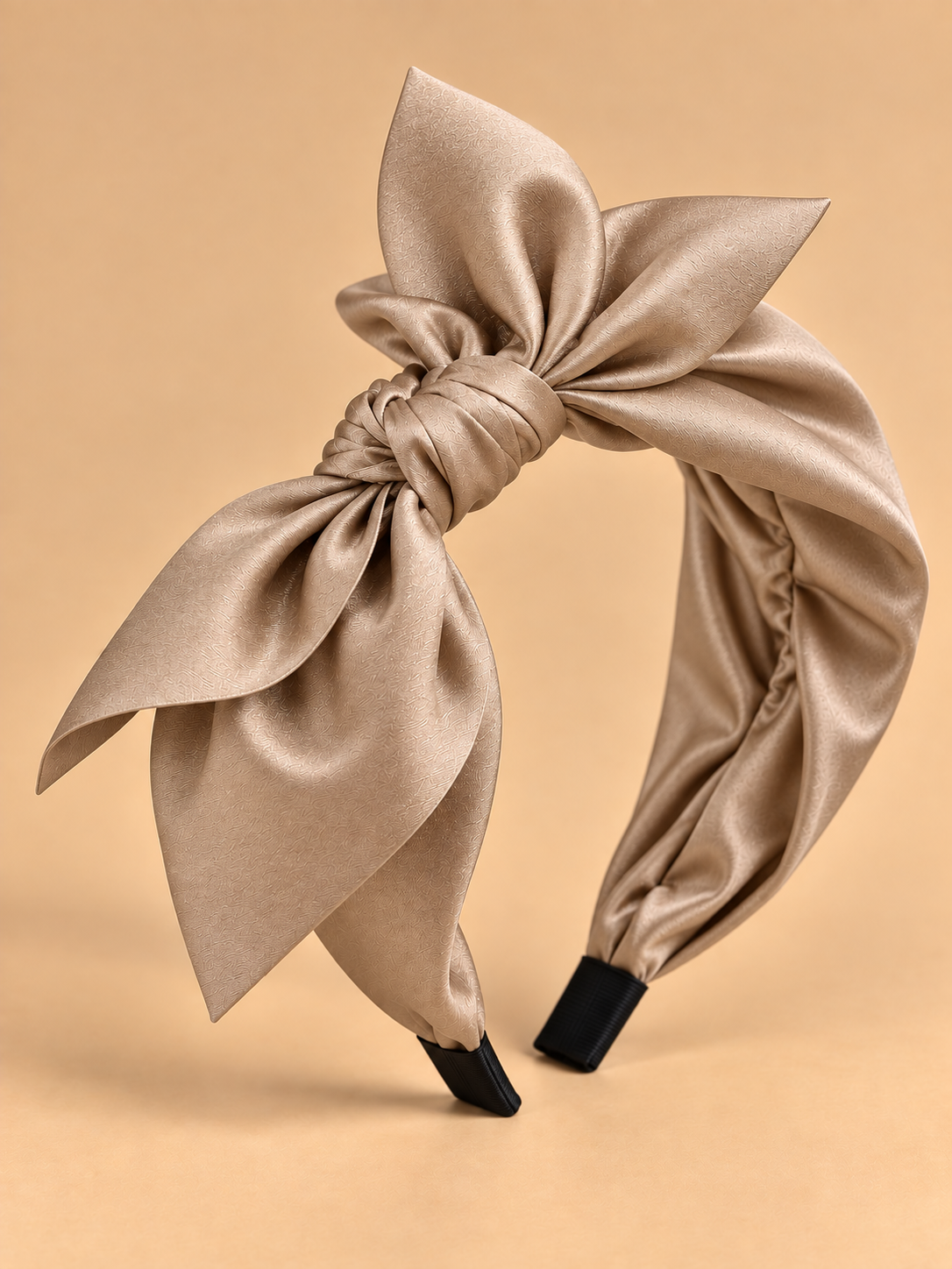 Beige glanzende stoffen haarband met strik op egale beige achtergrond