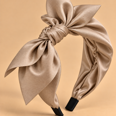 Beige glanzende stoffen haarband met strik op egale beige achtergrond