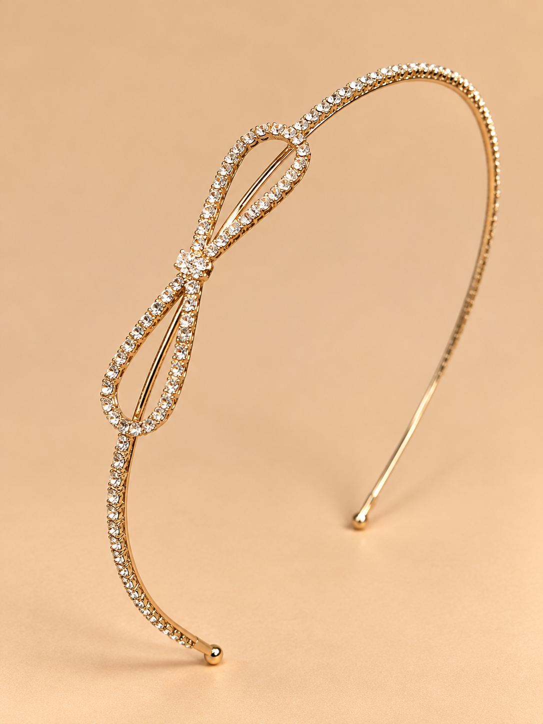 Goudkleurige haarband met strass en strik op egale beige achtergrond
