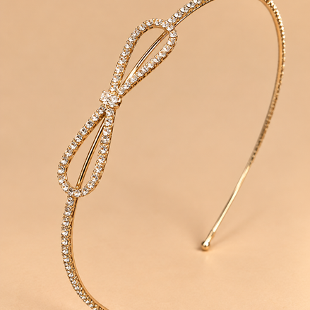 Goudkleurige haarband met strass en strik op egale beige achtergrond