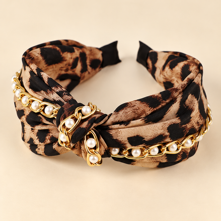 Luipaardprint knoop haarband met parels en goudkleurige ketting op egale beige achtergrond