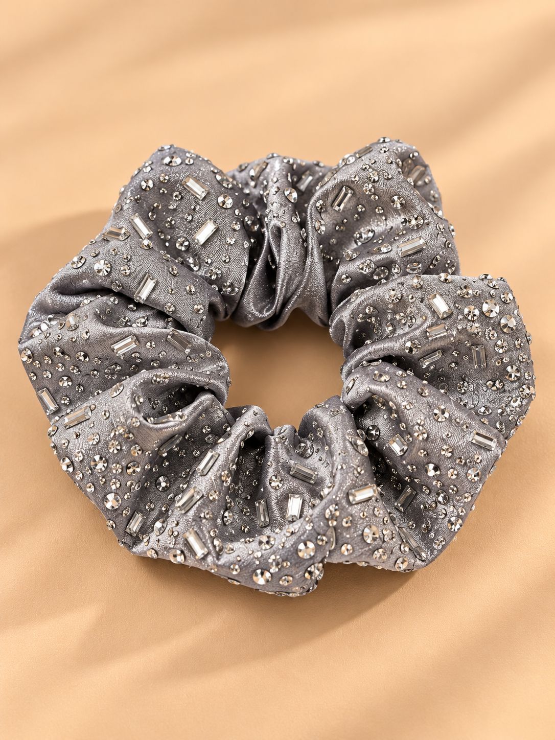 Luxe zilvergrijze scrunchie met strass steentjes op beige achtergrond