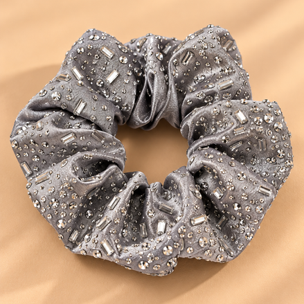 Luxe zilvergrijze scrunchie met strass steentjes op beige achtergrond