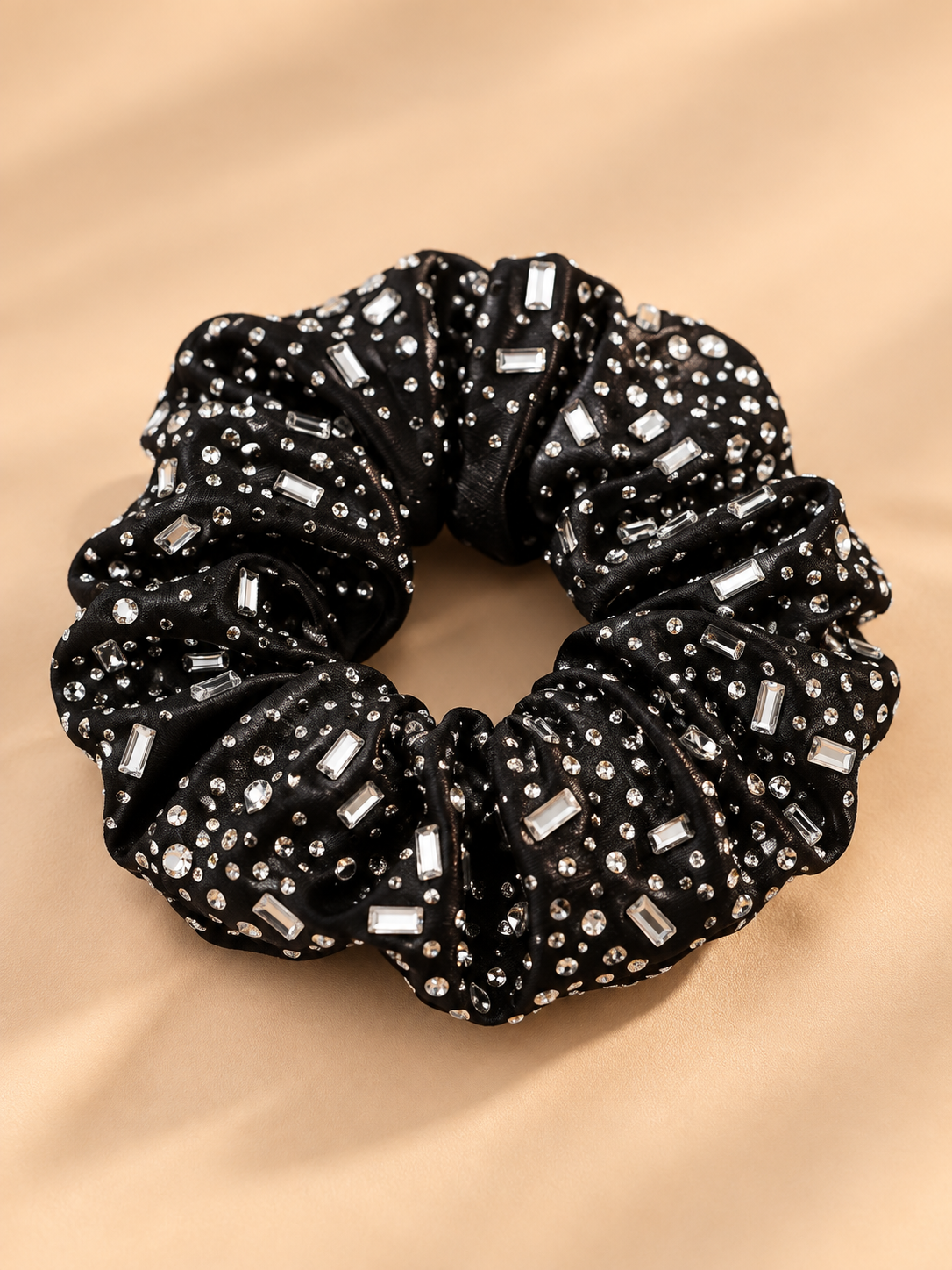 Luxe zwarte scrunchie met ronde en langwerpige strass steentjes op beige achtergrond