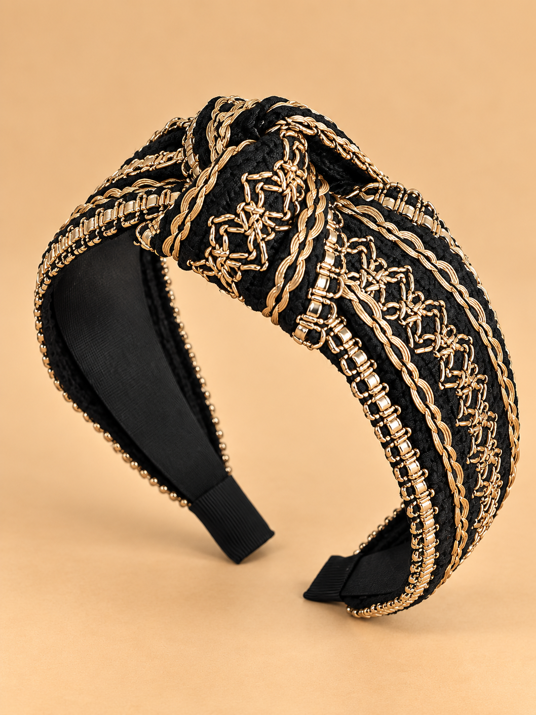 Luxe zwarte haarband met gouden details en knoop op egale beige achtergrond