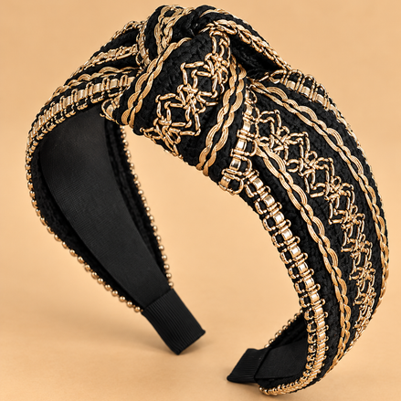 Luxe zwarte haarband met gouden details en knoop op egale beige achtergrond