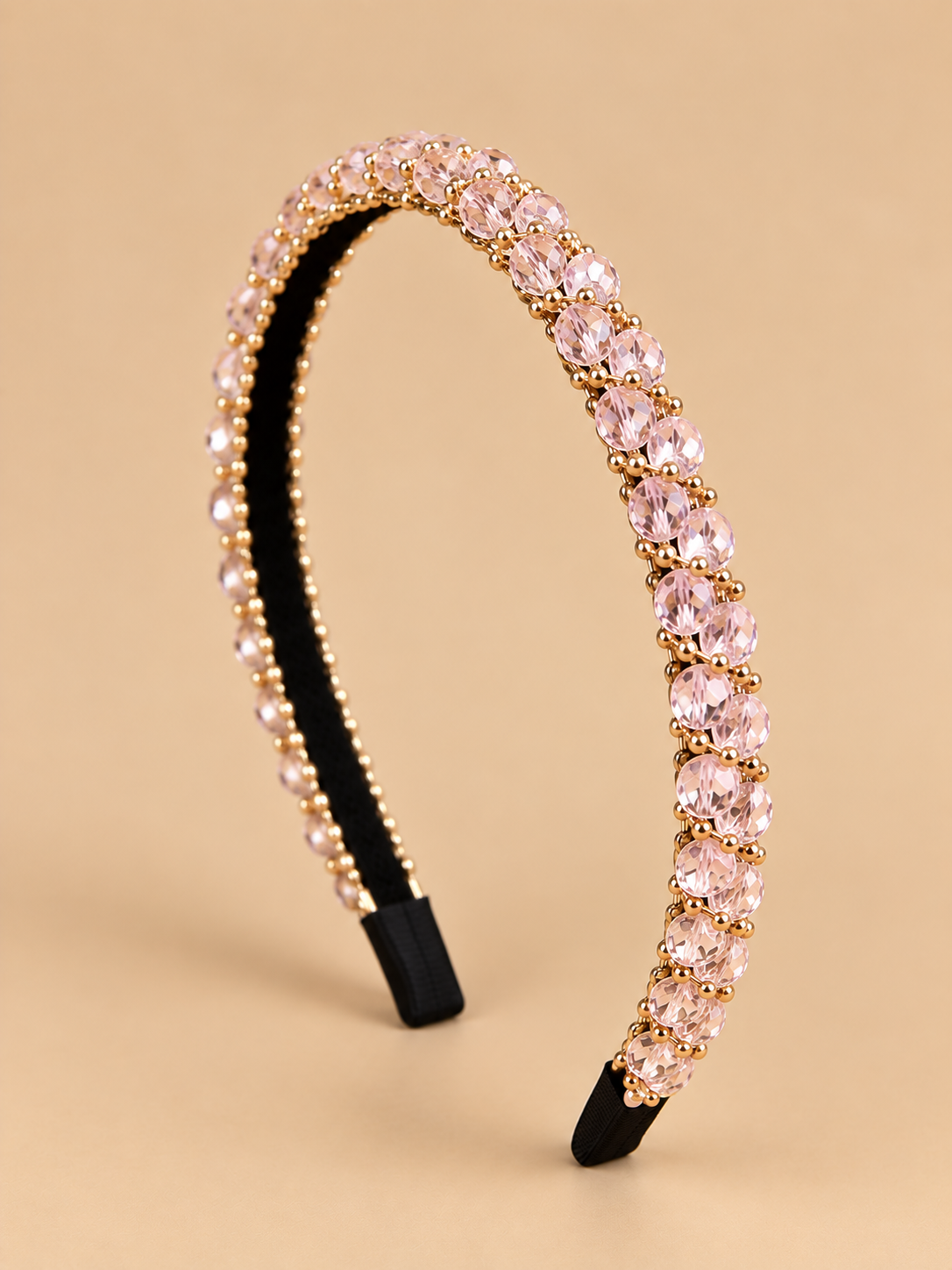 Smalle lichtroze kristal haarband met gouden details op egale beige achtergrond
