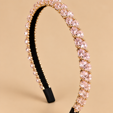 Smalle lichtroze kristal haarband met gouden details op egale beige achtergrond