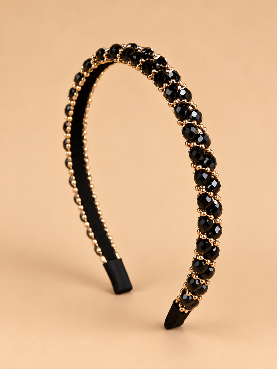 Smalle zwarte kristal haarband met gouden details op beige achtergrond