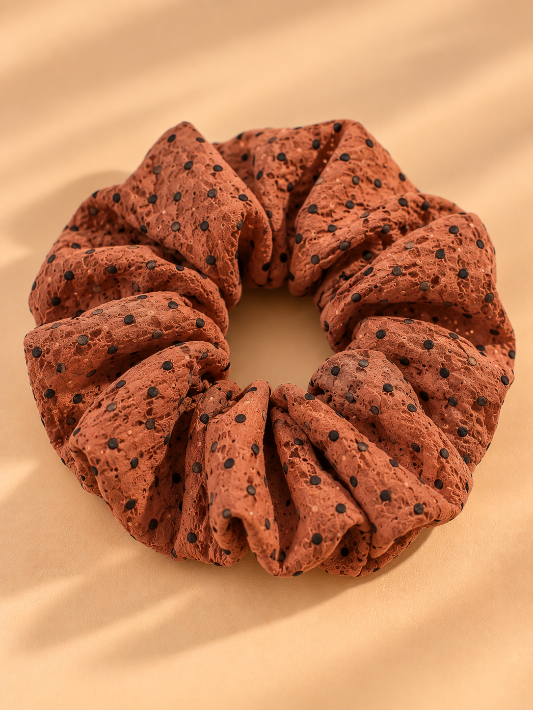 Bruine scrunchie met zwarte stippen op beige achtergrond
