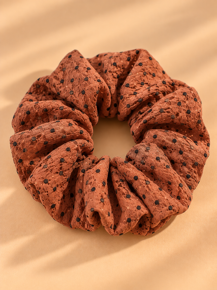Bruine scrunchie met zwarte stippen op beige achtergrond