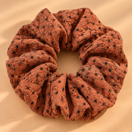 Bruine scrunchie met zwarte stippen op beige achtergrond