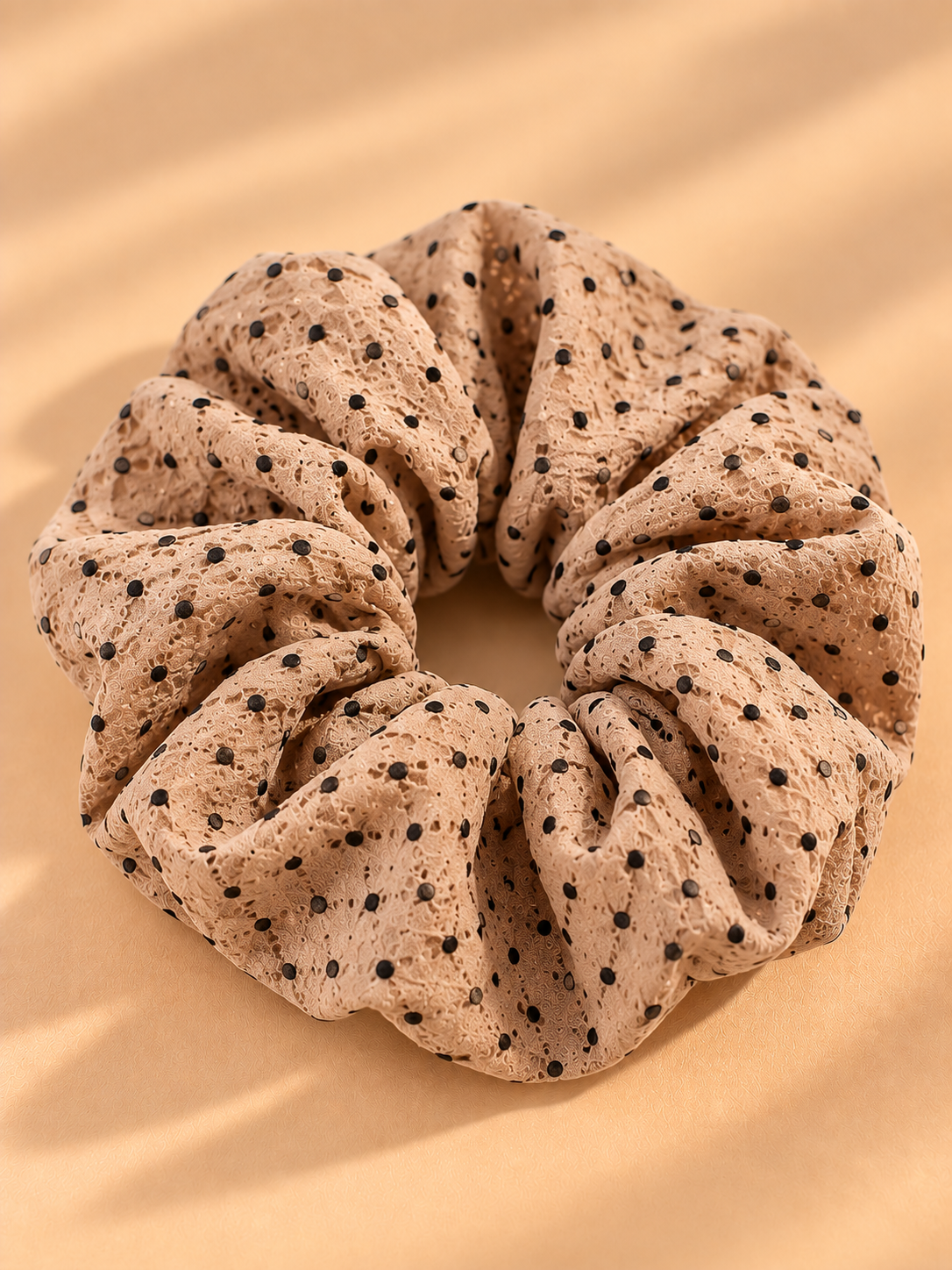 Lichtbruine scrunchie met zwarte stippen op beige achtergrond