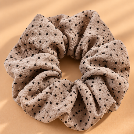 Taupe scrunchie met zwarte stippen op beige achtergrond