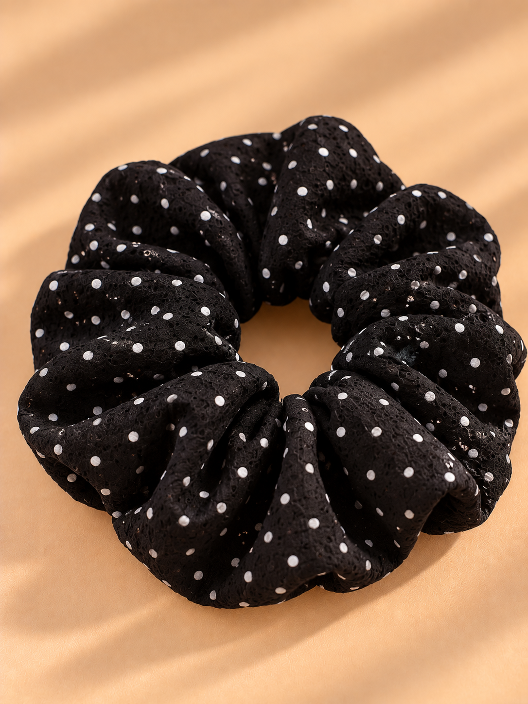 Zwarte scrunchie met witte stippen op beige achtergrond