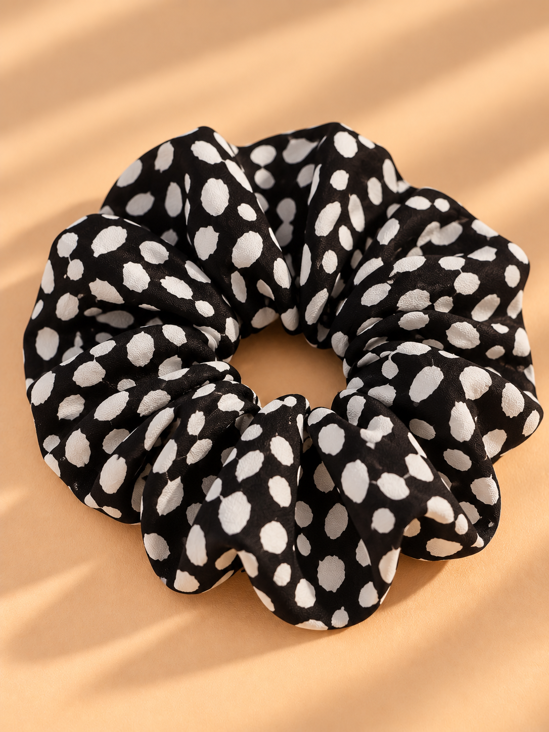 Zwarte scrunchie met witte dierenprint stippen op beige achtergrond