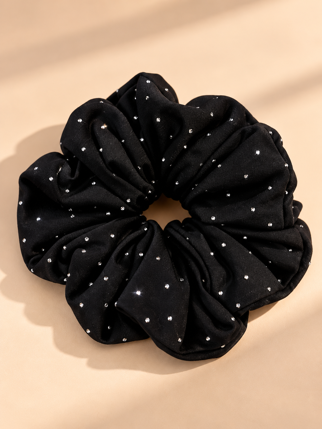 Luxe zwarte scrunchie met strass steentjes op beige achtergrond
